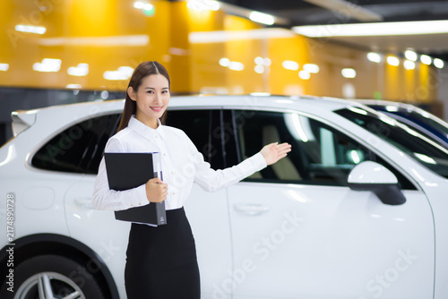 Fotografía Saleswoman presenting white SUV in car showroom