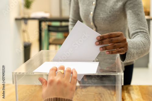 Принти на полотні People casting vote by placing ballot paper into transparent box at polling stat