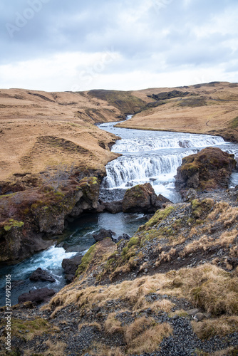 vertical photography of Skogaa River flows through tranquil grass fields before forming the famous Skogafoss waterfall on a cloudy day in March.