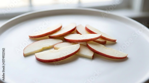 Fresh red apple slices arranged on white ceramic plate.