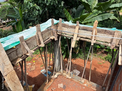 House construction site in Kerala, India, showing a partially built residential home with concrete columns, exposed brick walls, construction materials, and workers’ activity.
