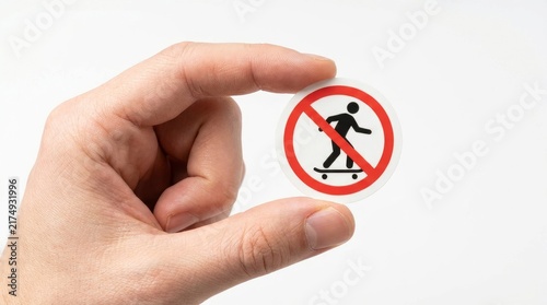 Hand holding a circular no skateboarding prohibition sign sticker