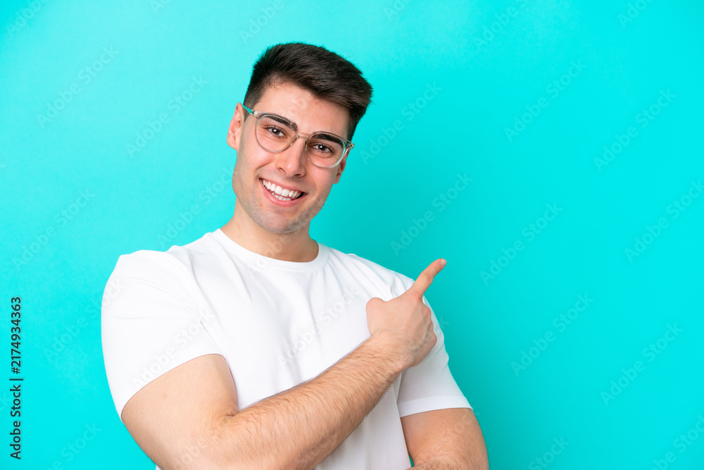 Fototapeta premium Young caucasian man isolated on blue background With glasses and pointing side