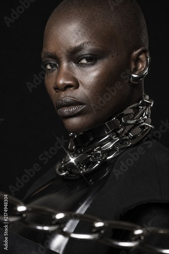 Bold Beauty: A striking portrait of a confident Black woman with a shaved head and captivating eyes, adorned with edgy jewelry, exudes an aura of power and sophisticated allure.