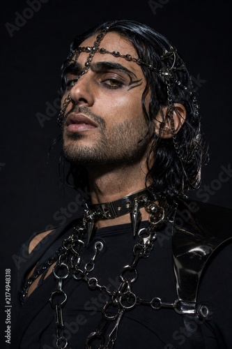 Mysterious Gaze: A striking portrait of a man with dark, flowing hair adorned with an intricate headpiece and a heavy, chained necklace, exuding an aura of enigmatic power and dark allure.