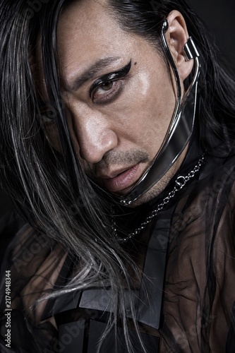 Man with Long Dark Hair and Dramatic Eyeliner: A close-up portrait of a man with flowing dark hair, striking eyeliner, and edgy accessories, conveying a sense of bold individuality and modern style.