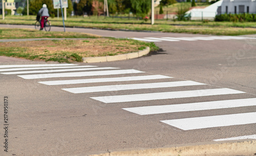 Pedestrian crossing marks white stripes on asphalt road surface. Marked crosswalk provides safety near urban street junction. Line crossing ensures road safety in quiet suburban neighborhood.