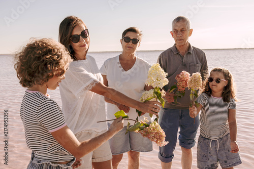 multigenerational family in shallow pink lake with hydrangea flowers, sunny summer day. grandparents parents and children enjoying quality time outdoors family bonding tourism