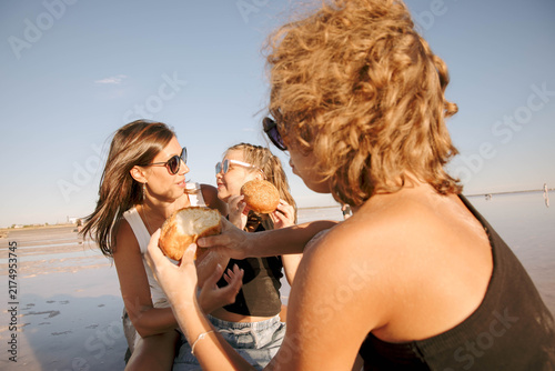 children enjoying fresh sesame bread on driftwood log with their mother at a pink salt lake, warm family picnic atmosphere, family bonding travel lifestyle and outdoor recreation