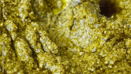 Spoon sliding through thick Italian pesto sauce with olive oil