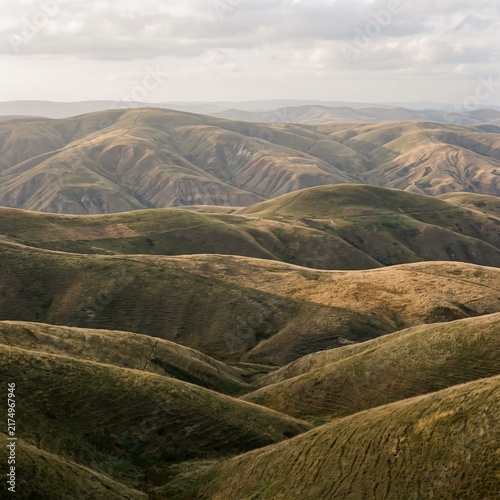 Rolling green hills landscape under cloudy sky, scenic mountain range with velvet texture, vast natural valley panorama