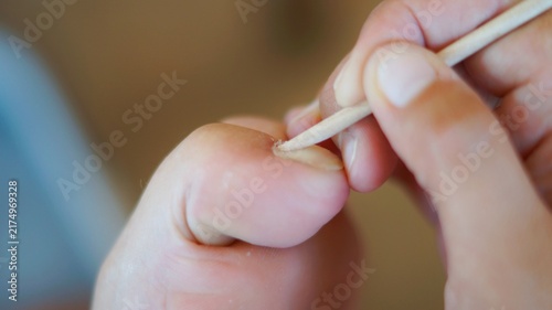 Close-up of a toenail being carefully cleaned around the cuticle with a small wooden manicure stick. The image represents precision, nail hygiene, attentive grooming, and routine personal self-care.