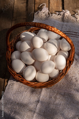 Foto Chicken eggs in a wicker large basket on wooden grunge table