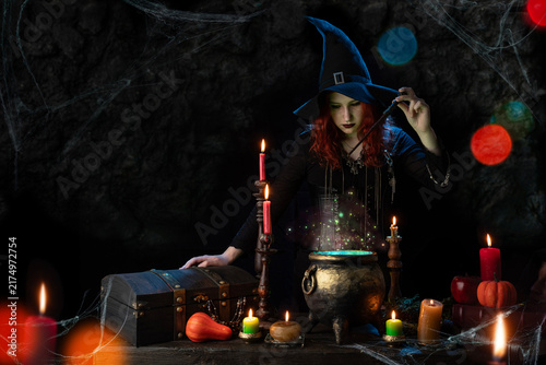 Fotografie Witch with magic wand casts spell, witch's cauldron, boiling magic potion, room with candles