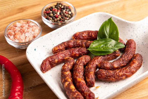 Obraz na płótnie Smoked kabanos sausages on white plate with fresh basil leaves close up