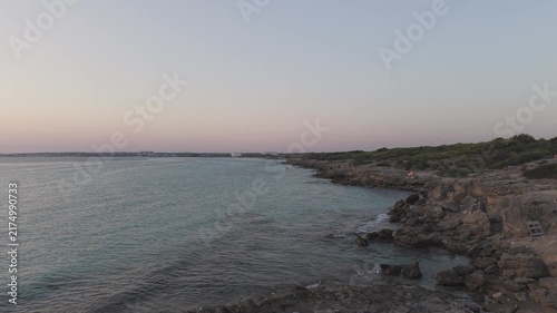 Aerial wide view of Punta della Suina coastline in Gallipoli, Salento, Italy. Drone shot of the turquoise Ionian sea, rocky shore, and pine forest at dusk.