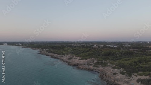 Cinematic high-angle drone flight over Punta della Suina natural park in Salento, Southern Italy. Scenic coastline with clear sea and pine forest during twilight.