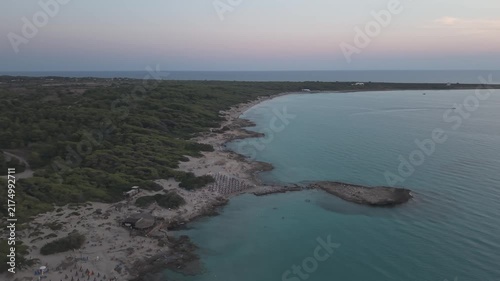 Aerial wide view of Punta della Suina coastline in Gallipoli, Salento, Italy. Drone shot of the turquoise Ionian sea, rocky shore, and pine forest at dusk.