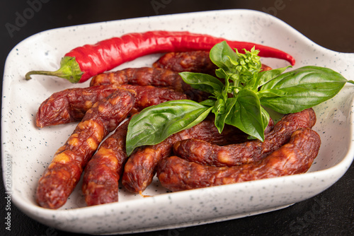 Obraz na płótnie Smoked kabanos sausages on white plate with fresh basil leaves close up