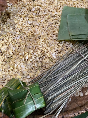 Konstfotografi Handmade tempe parcels in progress, tightly wrapped in green banana leaves and secured with bamboo sticks alongside peeled soybeans and traditional tools
