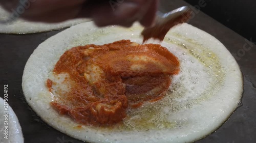 close up of benne dosa being spread with spicy masala on griddle