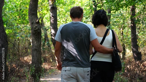 Happy couple walking along path at summer forest. Romantic pair going along trail at wild woodland. Lovers spending time together at nature. Concept of love and happiness. Slow motion