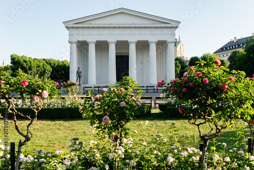 Beautiful white classical ancient greek style temple building with columns in a public park with blooming roses in Vienna Austria