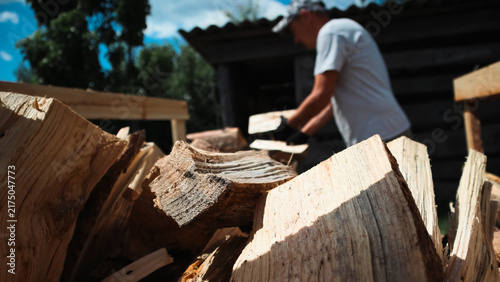 Fotografie Man wearing protective gloves stacking split wooden logs onto rack preparing fir