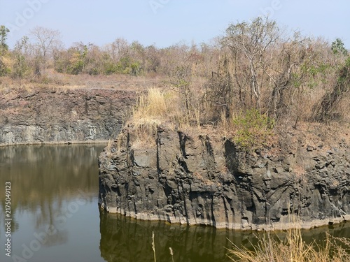 Foto Basalt Quarry Wall beside Water in Volcanic Outcrop
