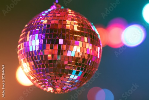 Faceted mirrored disco ball suspended in air reflecting magenta cyan and golden light with colorful bokeh circles blurred in background under dramatic nightlife illumination