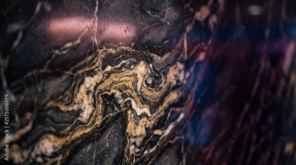 Fototapeta premium Abstract macro texture of luxurious black marble with swirling gold and white veins elegant stone background with soft purple rim lighting for sophisticated interior design and high-end surf