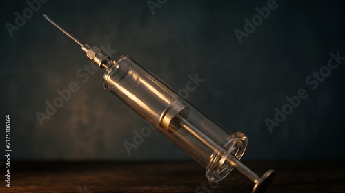 Vintage glass syringe with metal needle resting on a dark wooden surface in dramatic cinematic light for medical history or laboratory science concept