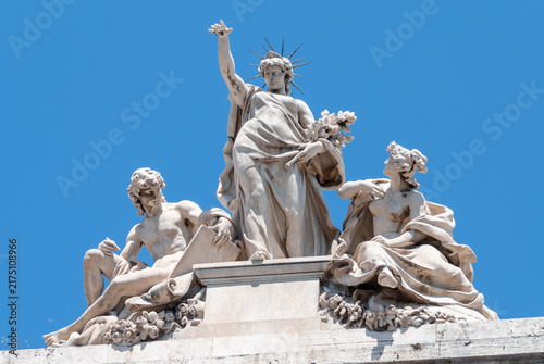 Принти на полотні Classical marble allegorical sculpture in Rome, Italy, depicting a radiant female figure with two reclining figures against a vivid blue sky