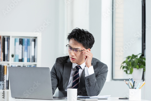 Confused businessman working on laptop in modern office