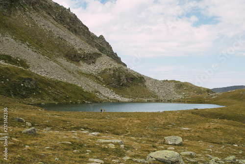 Fotografie Alpiner Bergsee mit zwei Wanderern in karger Hochgebirgslandschaft