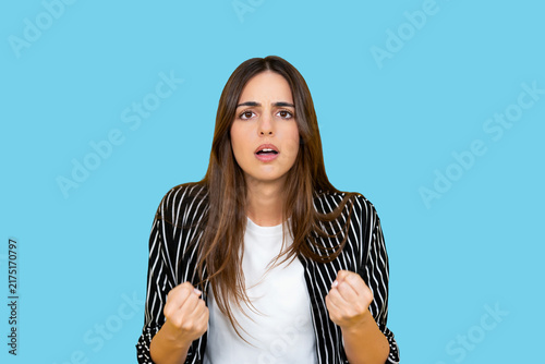 Fotografía Young woman standing on a blue background, clenching her fists and showing an an