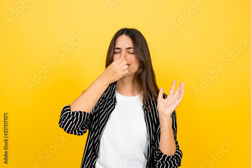 Foto Young woman closing eyes and pinching nose with fingers, reacting with disgust t