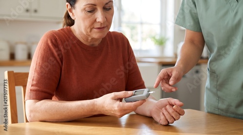 A nurse or caregiver is assisting an older woman with checking her blood glucose levels at home.