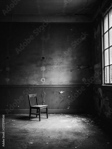 Single wooden chair in a dark, dilapidated room with window light