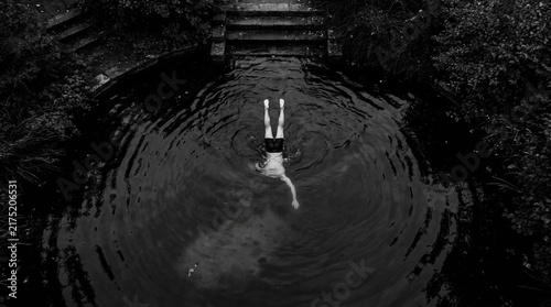 Overhead view of a person diving headfirst into dark water, creating ripples, with steps and trees in the background.