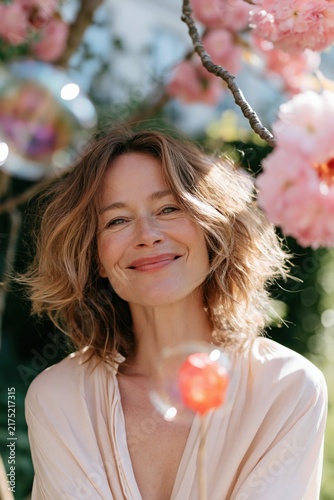 Smiling woman among pink cherry blossoms with soft sunlight for spring background and floral lifestyle imagery