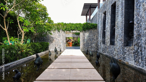 Konstfotografi Stone-walled walkway over a tranquil water feature adorned with artistic bird sc