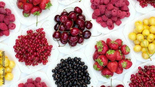 Rotating top view of assorted fresh summer berries including strawberries cherries raspberries and currants on white plates
