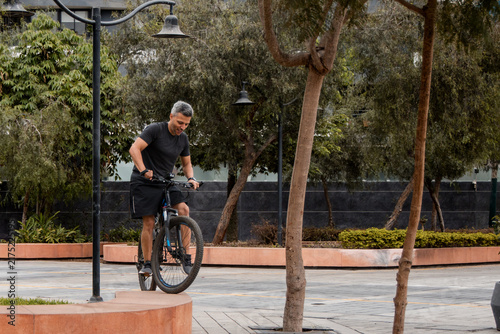 Man Smiling While Cycling Through a City Plaza