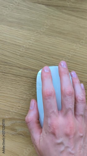 Hand clicking the left button of a computer mouse. Vertical shot of fingers navigating on a wooden desk. Close-up moment of everyday computer interaction..