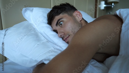 Foto Young man suddenly waking up in bed with surprised expression in modern hotel room or home interior