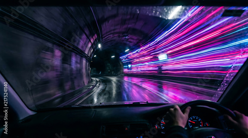 Car driving through neon tunnel with light streaks blur effect for nightlife travel.