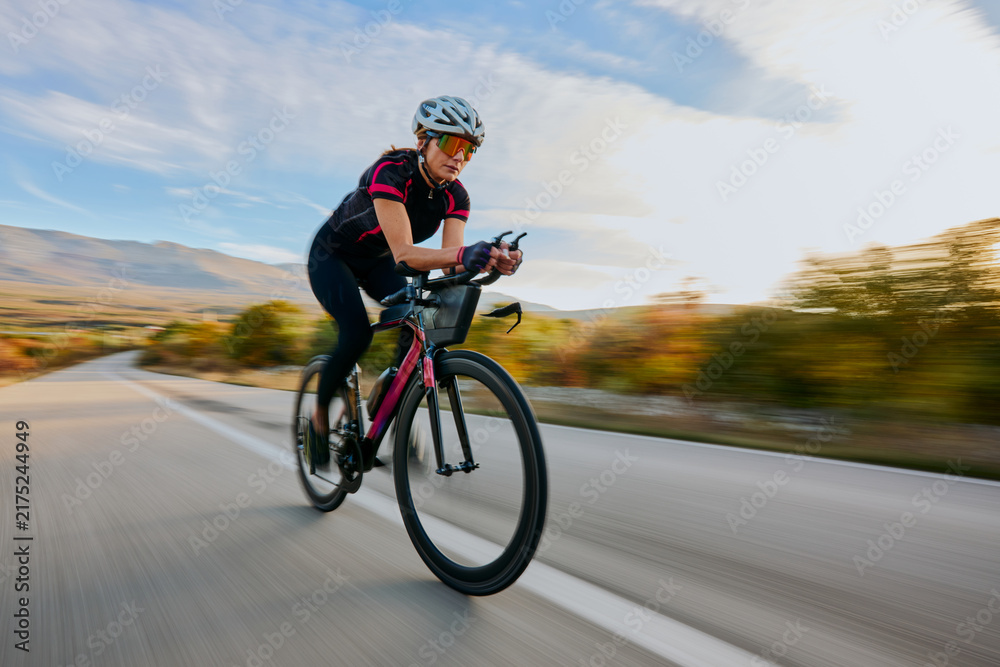 Naklejka premium Female Cyclist Riding Fast On Road Bike Through Countryside During Outdoor Training
