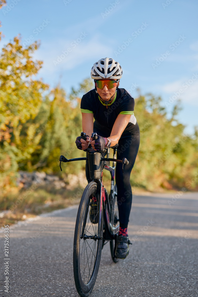Naklejka premium Female Cyclist Riding Road Bike in Aerodynamic Position on Quiet Country Road During Training