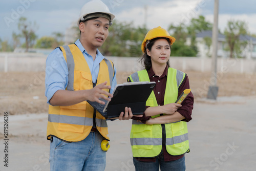 Asian male engineer holding tablet and pointing at construction site during inspection with colleague